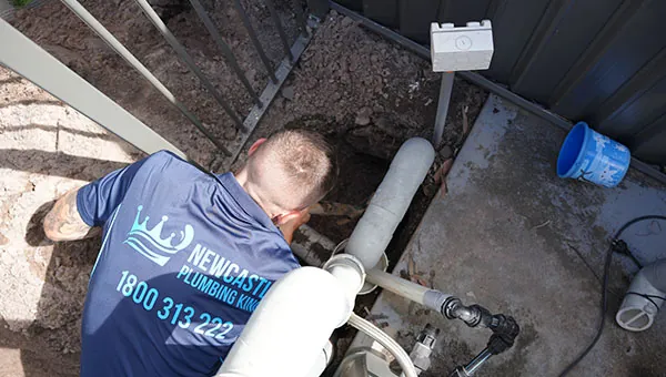Plumber repairing an exposed pipe in a trench